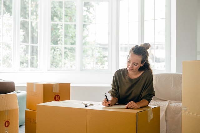 a tenant in a green crewneck sweater smiles while labelling a moving box to prepare to move into their new rental home